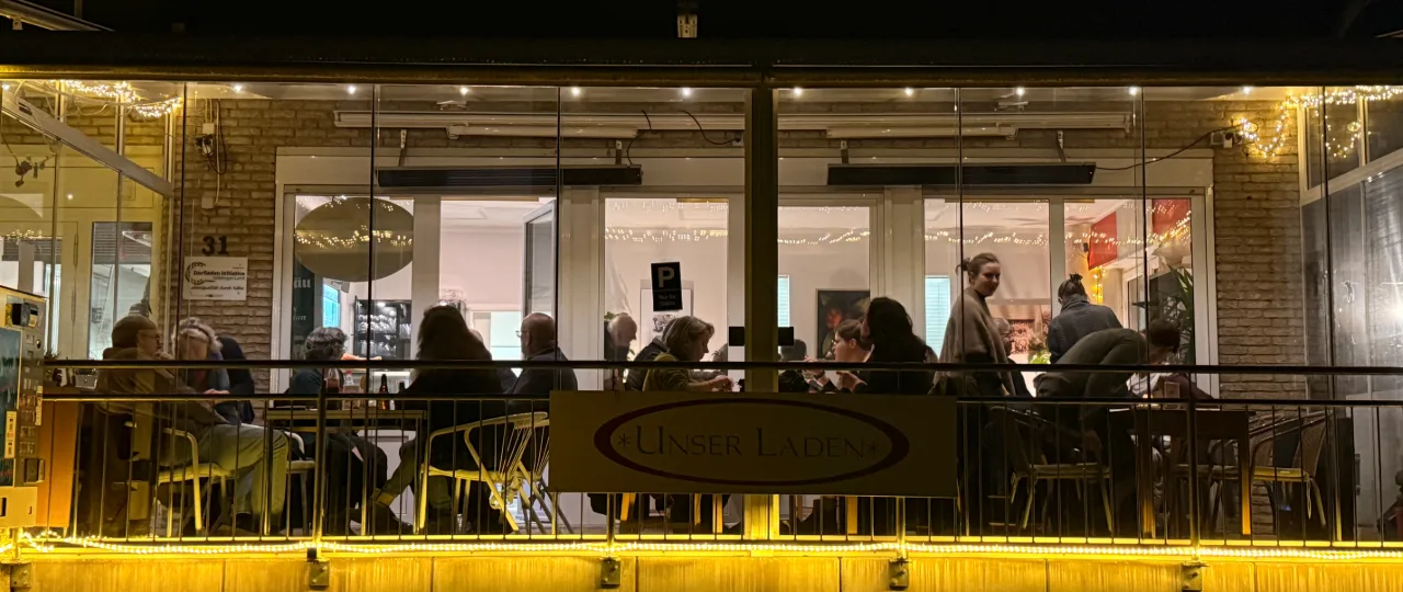 Die beleuchtete Terrasse des Berg-Cafés bei Nacht, dahinter der volle Gastraum